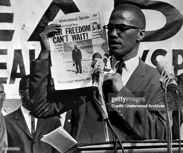 American Muslim leader and activits Malcolm X holds up an issue of the Muhammad Speaks newspaper during a rally, New York, New York, July 27, 1963.