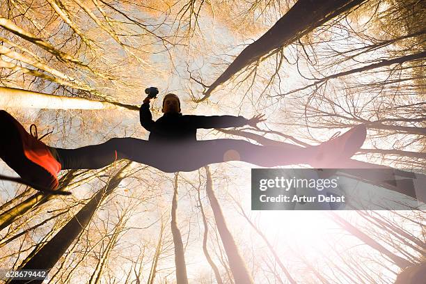 original low point of view of a guy jumping in a beautiful beech forest outdoor on autumn season in the montseny nature reserve of catalonia region with nice vanishing point of the long trees. - mens long jump stockfoto's en -beelden