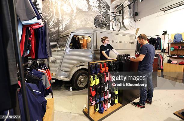 An employee serves a customer at the cash desk as a vintage Citroen H Van stands behind at the Rapha Racing Ltd. Cycle club on Brewer Street in...