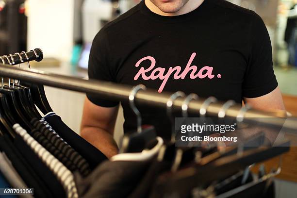 An employee wearing a branded t-shirt arranges a rack of clothing on display at the Rapha Racing Ltd. Cycle club on Brewer Street in London, U.K., on...