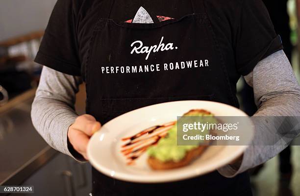 An employee wearing a branded t-shirt carries a customer's food order in the cafe area at the Rapha Racing Ltd. Cycle club on Brewer Street in...