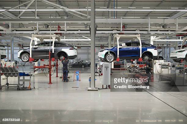 Employees fit rear axles to Tesla Model X sports utility vehicles as they sit in elevated cradles during assembly for the European market at the...