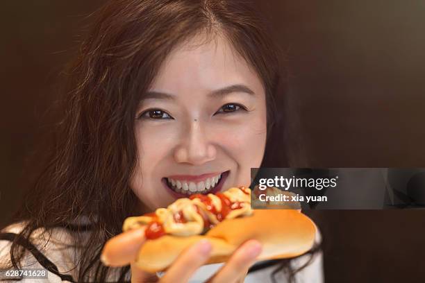 close up of a young woman eating a hot dog - asian eating hotdog stock-fotos und bilder