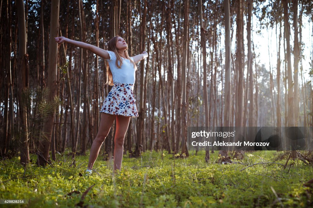 A girl with open arms is standing on a clearing in the forest