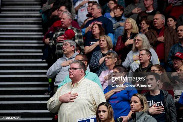 Members of the audience stand for The Pledge of Allegiance before President-elect Donald Trump takes the stage at the DeltaPlex Arena, December 9,...