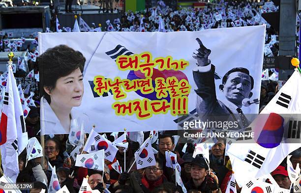 Supporters of scandal-hit President Park Geun-Hye hold a large banner with a slogan that shows portraits of President Park and her father, former...