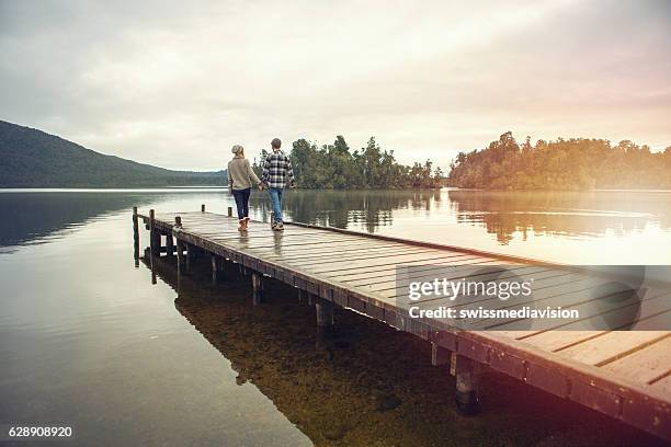 young couple walking on wooden pier above lake - couple jetty stock pictures, royalty-free photos & images