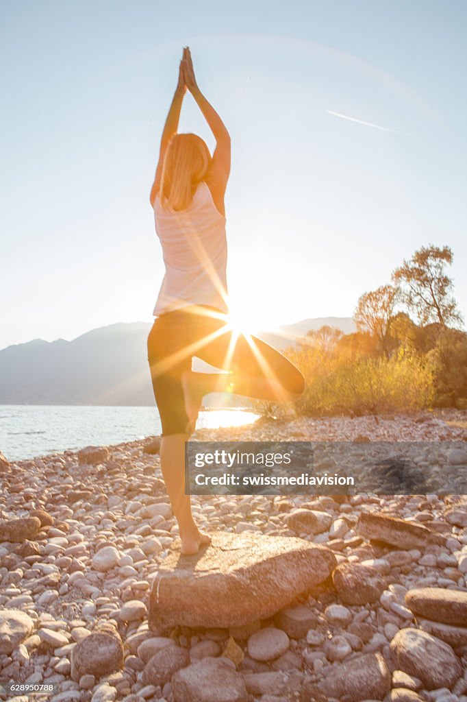 Young woman by the lake exercising yoga at sunrise