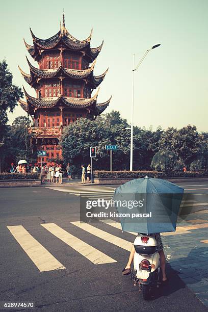 traditional chinese pagoda with the back of a woman riding electronic bicycle in the city in day - chengdu stock pictures, royalty-free photos & images