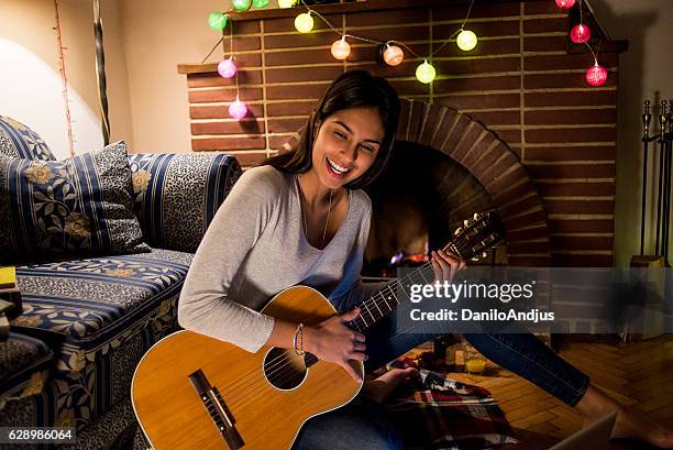 happy young woman playing the guitar at home - hot latin nights stock pictures, royalty-free photos & images