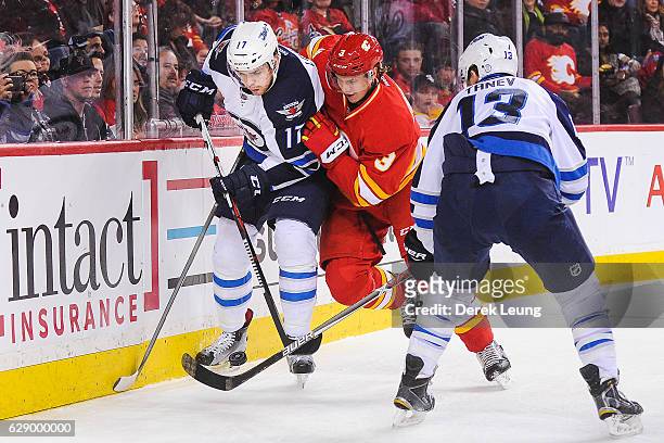 Jyrki Jokipakka of the Calgary Flames fights Adam Lowry of the Winnipeg Jets for the puck during an NHL game at Scotiabank Saddledome on December 10,...