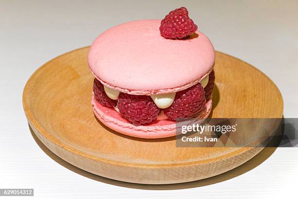 close-up of fresh pink raspberry macaroon with mint leaves decoration on wood plate - macaroon photos et images de collection