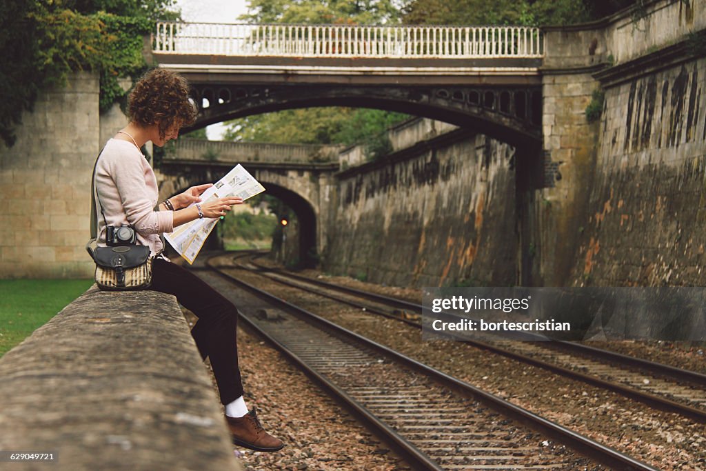 Woman Sitting On Retaining Wall Reading Newspaper By Railroad Tracks