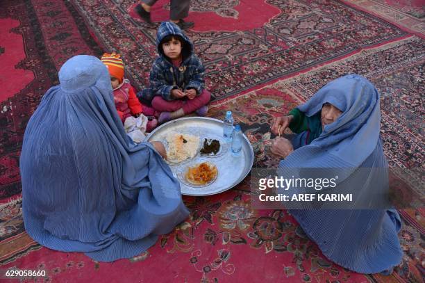 Afghan women and children eat during celebrations marking the birth anniversary of the Prophet Mohammed in Herat on December 11, 2016. - The birth of...