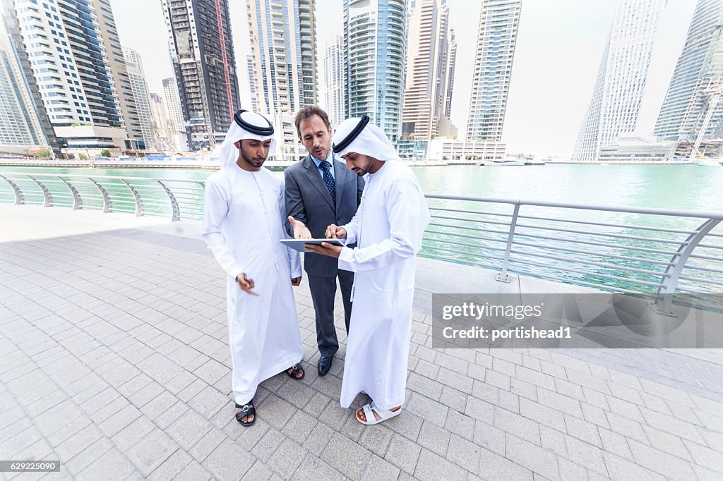 Three businessmen talking on street and using digital tablet