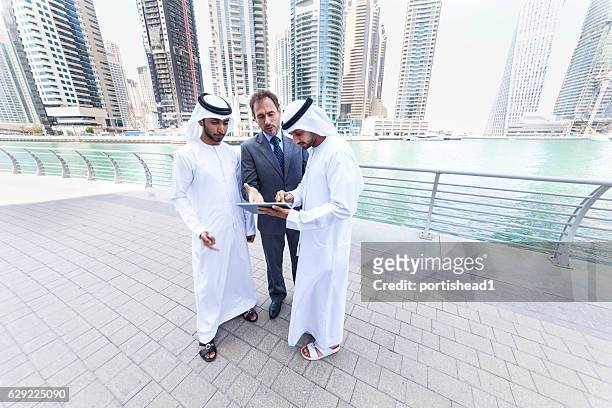 three businessmen talking on street and using digital tablet - perzische golfstaten stockfoto's en -beelden