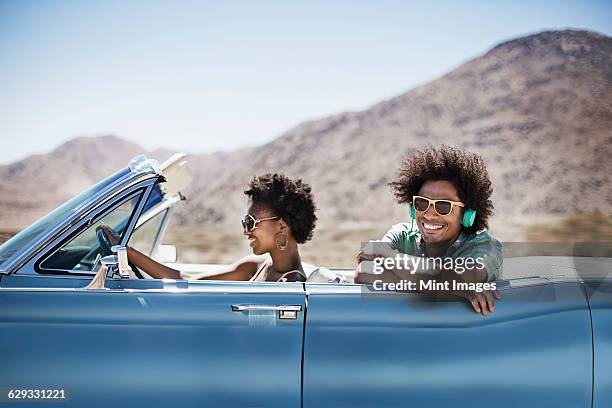 a young couple, man and woman in a pale blue convertible on the open road  - convertible car fotografías e imágenes de stock