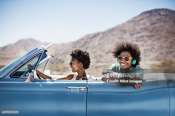 a young couple, man and woman in a pale blue convertible on the open road  - spider foto e immagini stock