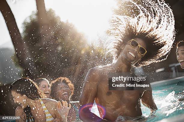 a group of young men and women in the swimming pool at the end of a hot day. - man splashed with colour fotografías e imágenes de stock