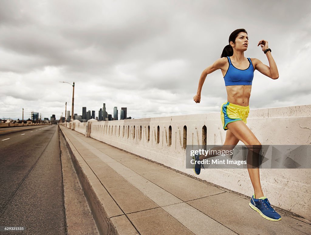 A woman running along an urban road pumping her arms and stretching her legs.