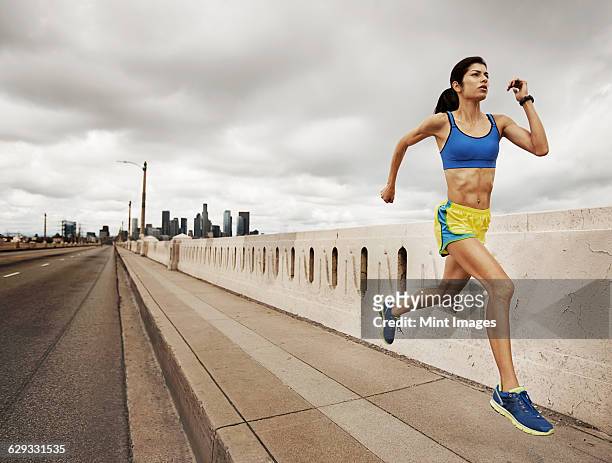 a woman running along an urban road pumping her arms and stretching her legs. - jogster stockfoto's en -beelden
