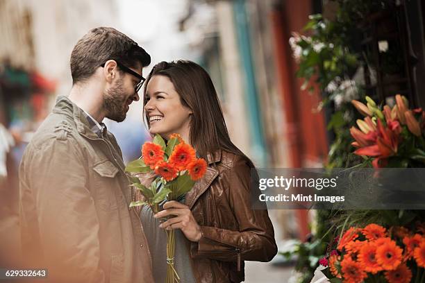 a man and woman by a flower stall in the city, holding a bunch of bright red flowers.  - flower stall imagens e fotografias de stock