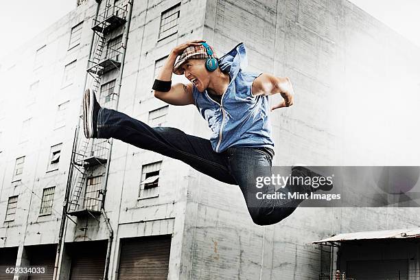 a young man doing a karate kick, one leg outstretched and one leg bent up, wearing earphones. - 空手　蹴る　not子供 ストックフォトと画像
