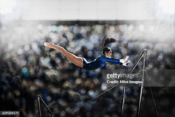 a female gymnast, a young woman performing on the parallel bars, in mid flight reaching towards the top bar.  - barras paralelas barra de ginástica - fotografias e filmes do acervo