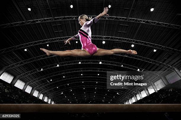 a young woman gymnast performing on the beam, balancing on a narrow piece of apparatus. - gymnast stock pictures, royalty-free photos & images