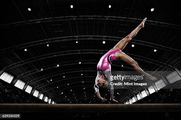 a young woman gymnast performing on the beam, balancing on her hands on a narrow piece of apparatus. - acrobat imagens e fotografias de stock