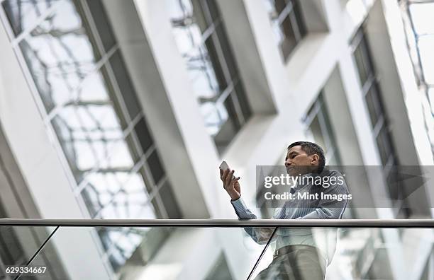 a man checking his smart phone in a large airy building with windows. - mobility windows phone stock pictures, royalty-free photos & images