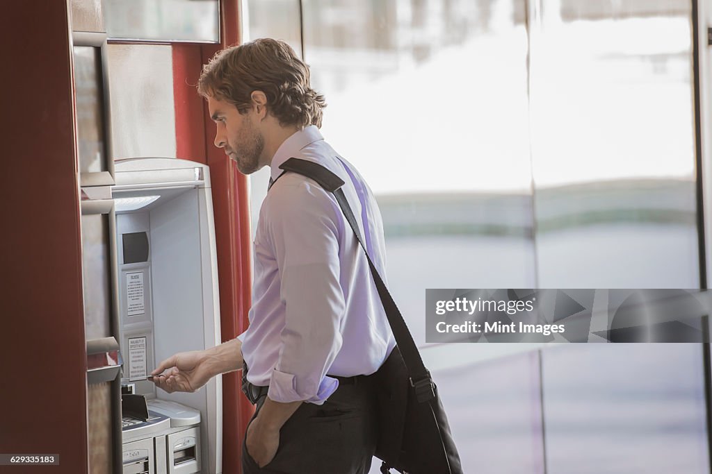 A man with a laptop bag using an ATM, a cash machine on a city street. 