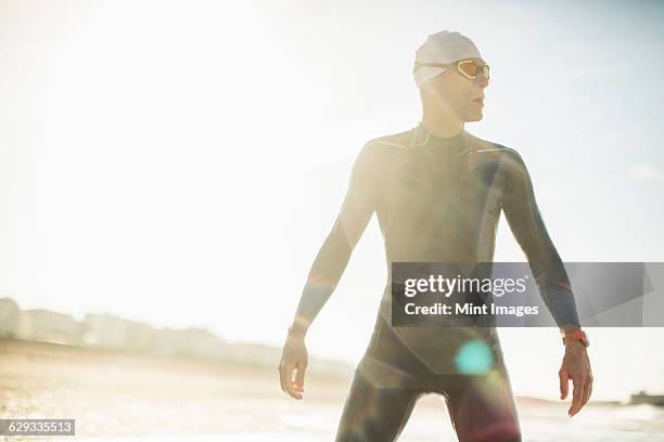 a swimmer in a wet suit, swimming hat and goggles on a beach.  - wetsuit stock pictures, royalty-free photos & images