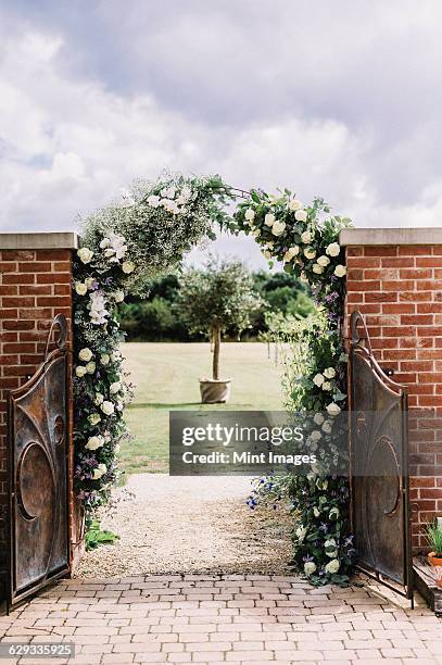 a door in a wall, and a white rose arch in a garden, with a view to a sundial.  - garden gate rose stock pictures, royalty-free photos & images
