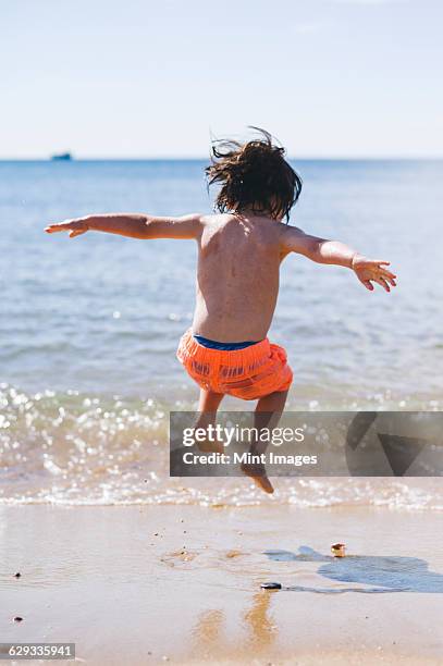 a boy in swimming trunks jumping over waves on the sea shore. - zwembroek stockfoto's en -beelden