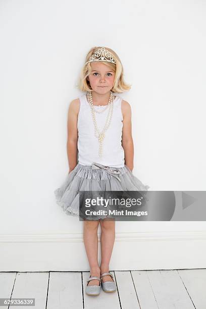 young girl wearing a tiara and a pearl necklace, posing for a picture in a photographers studio. - kids tiara stock pictures, royalty-free photos & images