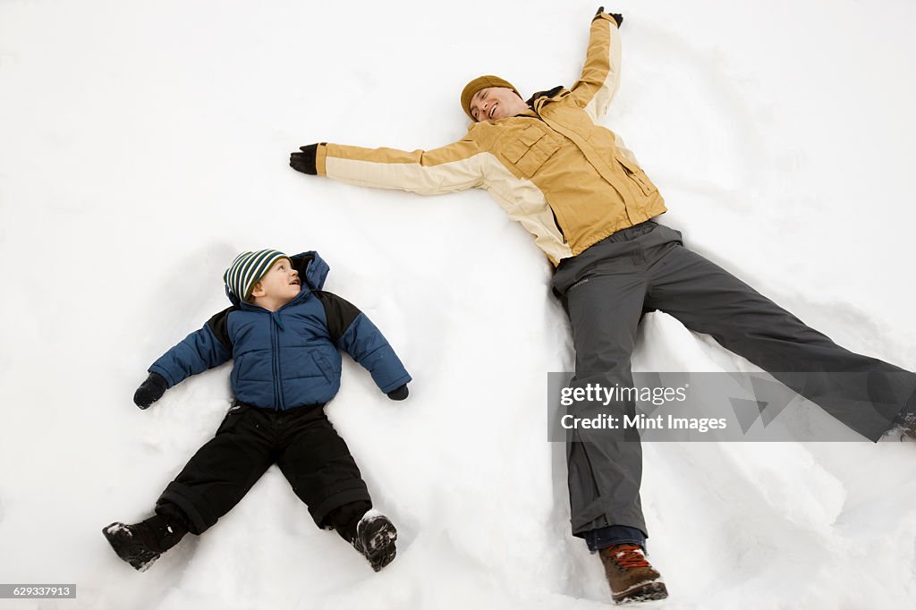 Two people, a man and a child lying in the snow make snow angel shapes. 