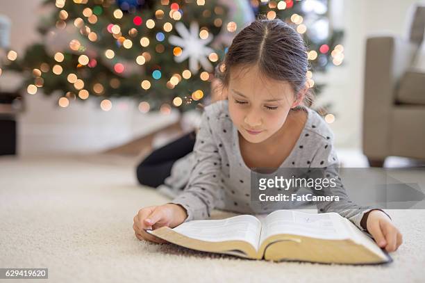 ethnische mädchen lesen ein dickes buch am weihnachtsbaum - young thick girls stock-fotos und bilder