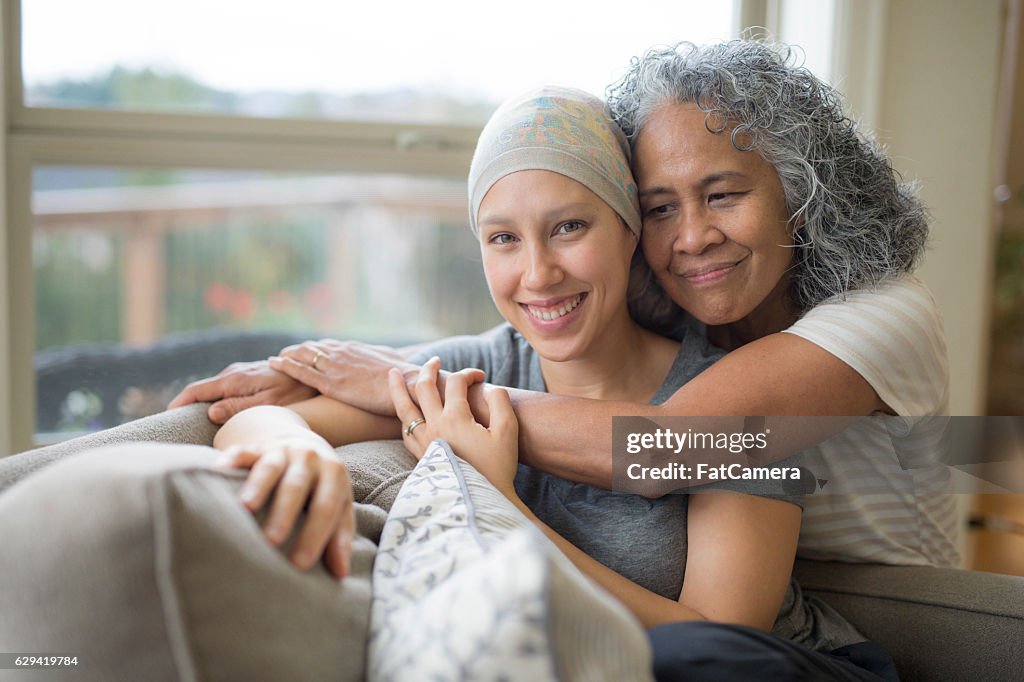 Ethnische junge erwachsene Krebspatientin von ihrer Mutter umarmt