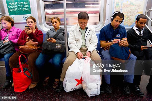 New York. Queens. Seated subway passengers on the E Train all using their mobile cell phones but not making telephone voice calls.