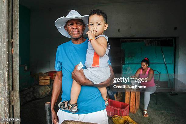 Local man holds his young grandson while awaiting costumers, inside his small shop selling fruits and vegetables. A typical scene from daily life in...