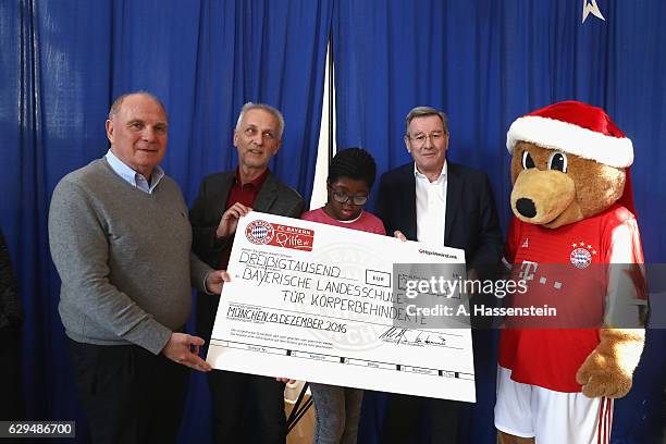 Uli Hoeness , President of FC Bayern Muenchen hands over a cheque as he and Karl Hopfner visit the School For Disabled People on December 13, 2016 in...