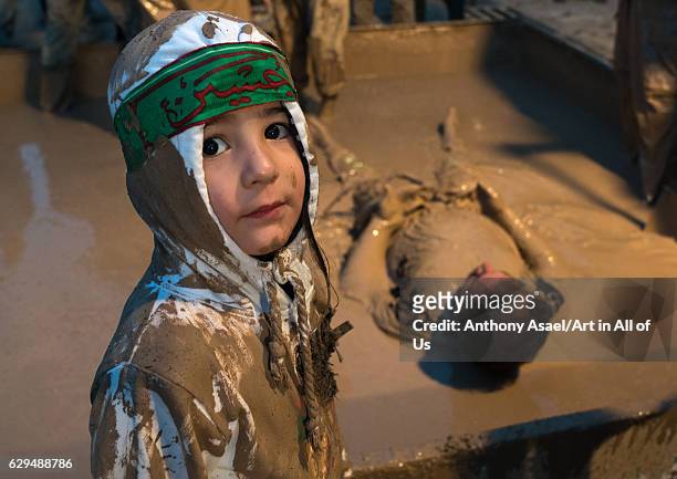 An iranian shiite muslim child in front of a mud pond while his father takes part in the Kharrah Mali ritual during the Ashura ceremony, Lorestan...