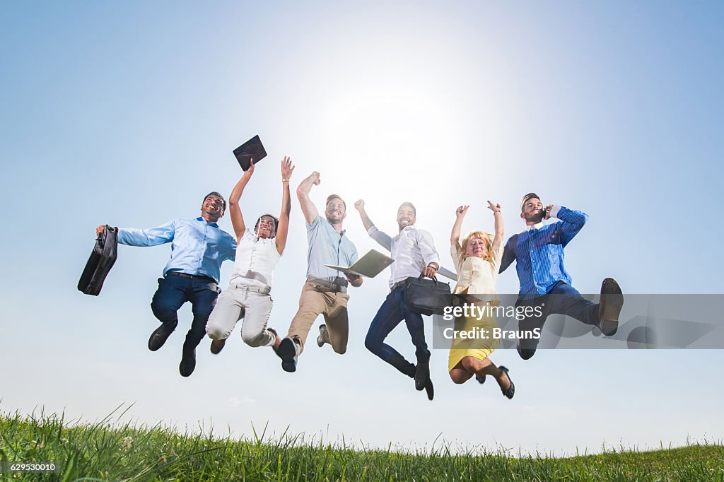 Below view of large business team jumping of joy outdoors.