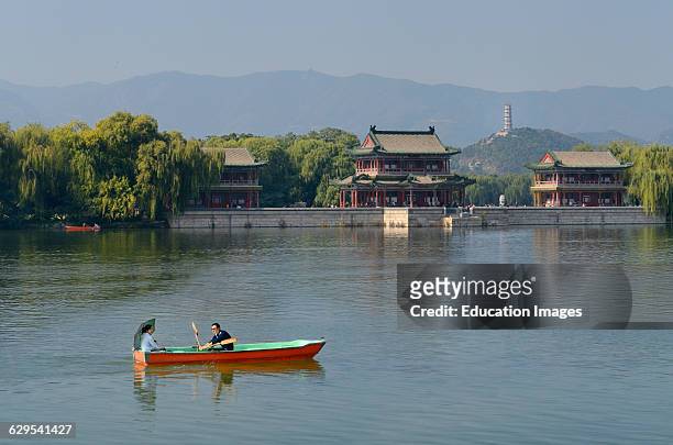 Couple rowing past the Pavilion of Bright Scenery with Jade Peak Pagoda on Kunming Lake Summer Palace Beijing.