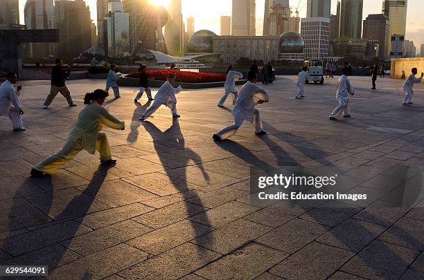 Long shadows of group doing Tai Chi exercises on the Bund at dawn with Shanghai skyline China.