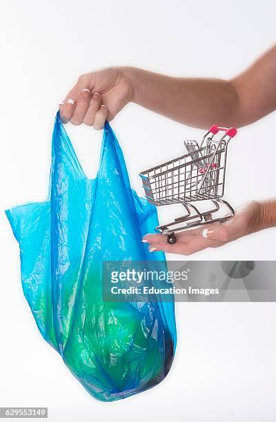 Woman holding tiny supermarket trolley and plastic shopping bag.