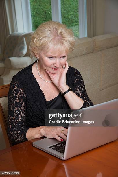 Elderly woman in a black dress using a laptop computer.