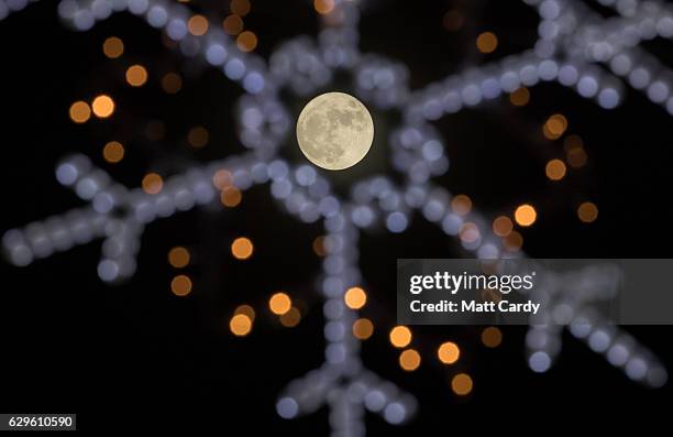 Clouds clear to allow a view of the final full moon of the year, a so called 'Cold Moon', as it appears behind Christmas lights decorating Penzance...