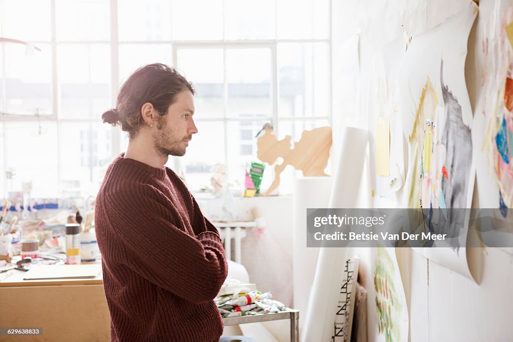 Male artist looks thoughful at painting on wall.